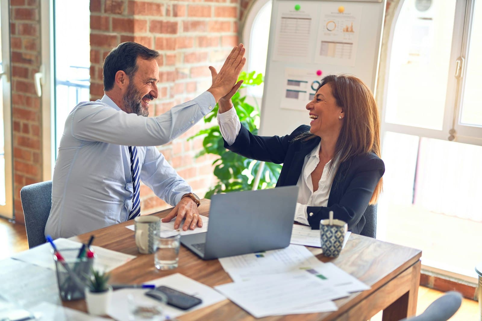 Two colleagues high-fiving across a desk in a bright office