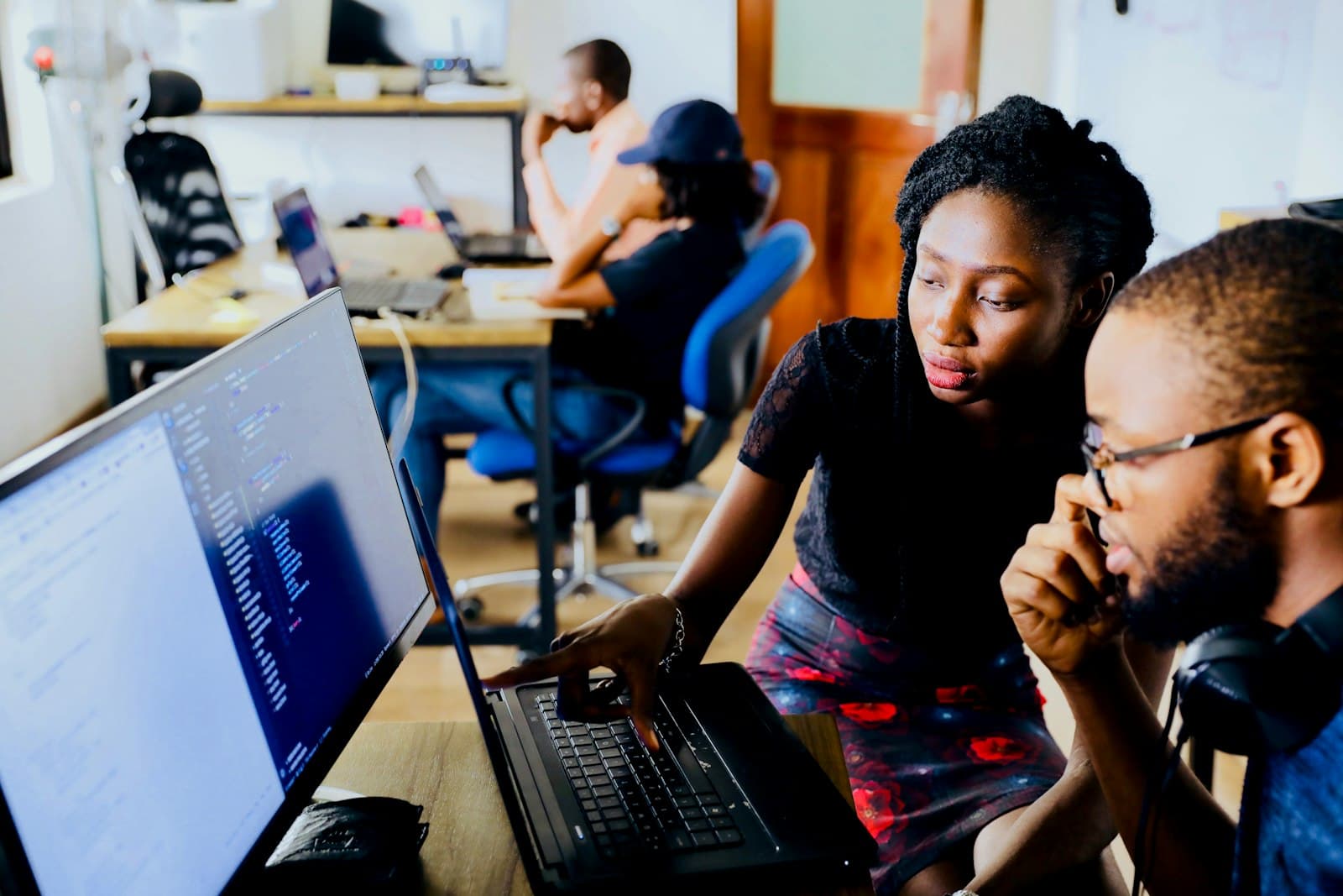 Two colleagues reviewing work on a laptop in a busy office